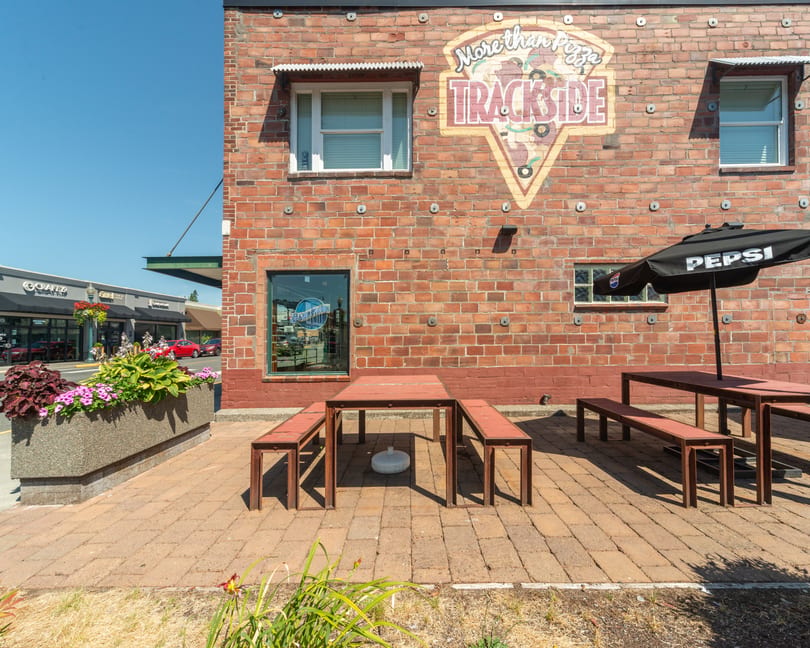 Trackside Pizza's brick exterior with outdoor seating, a Pepsi umbrella, and a large pizza mural.